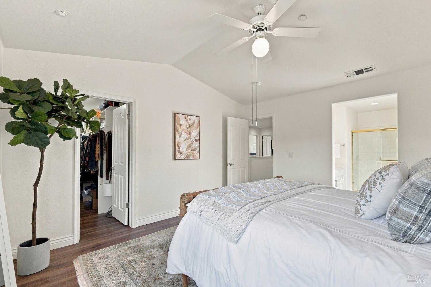 Furnished bedroom with a white bed, ceiling fan, and open closet and bathroom doors.