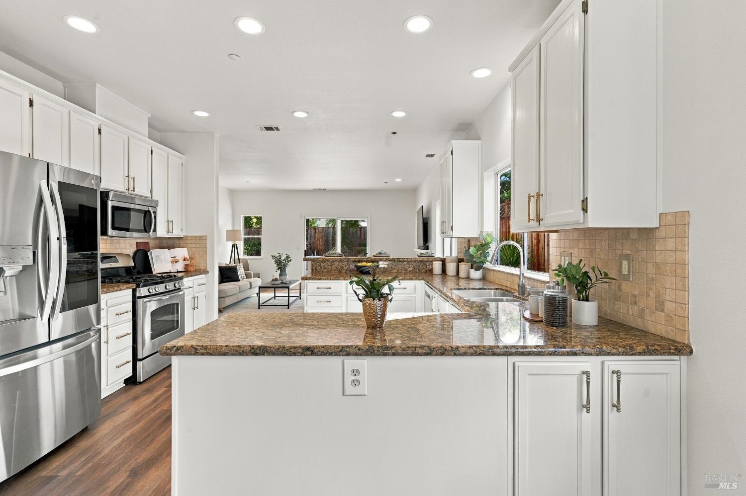 Bright kitchen with white cabinets, stainless appliances, and a large granite island.