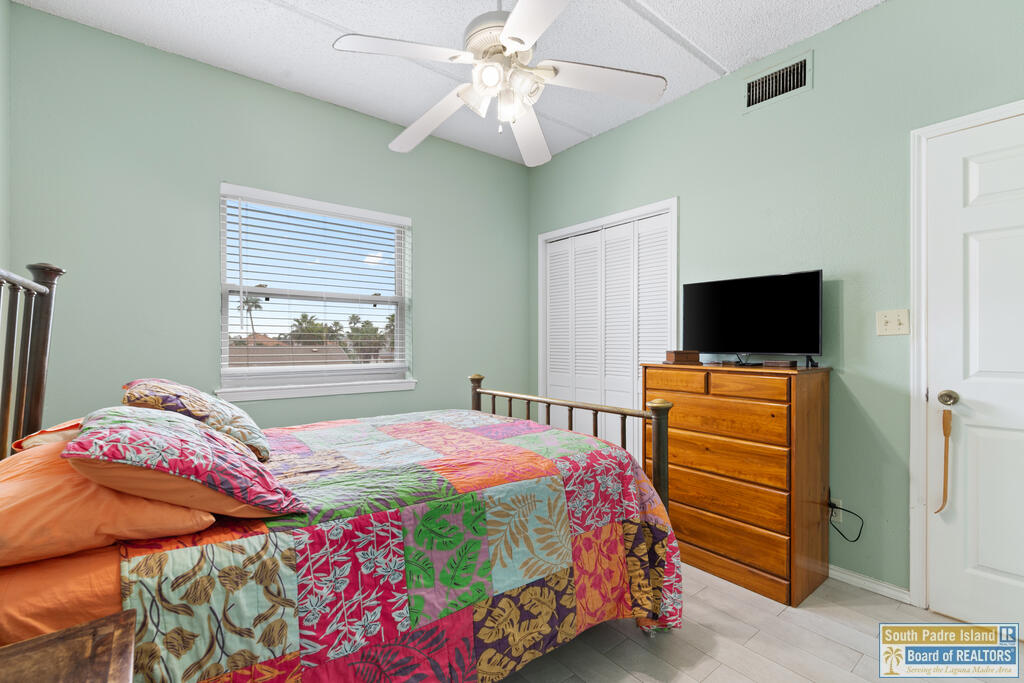 Bedroom with a colorful patchwork quilt, ceiling fan, and dresser with a television.