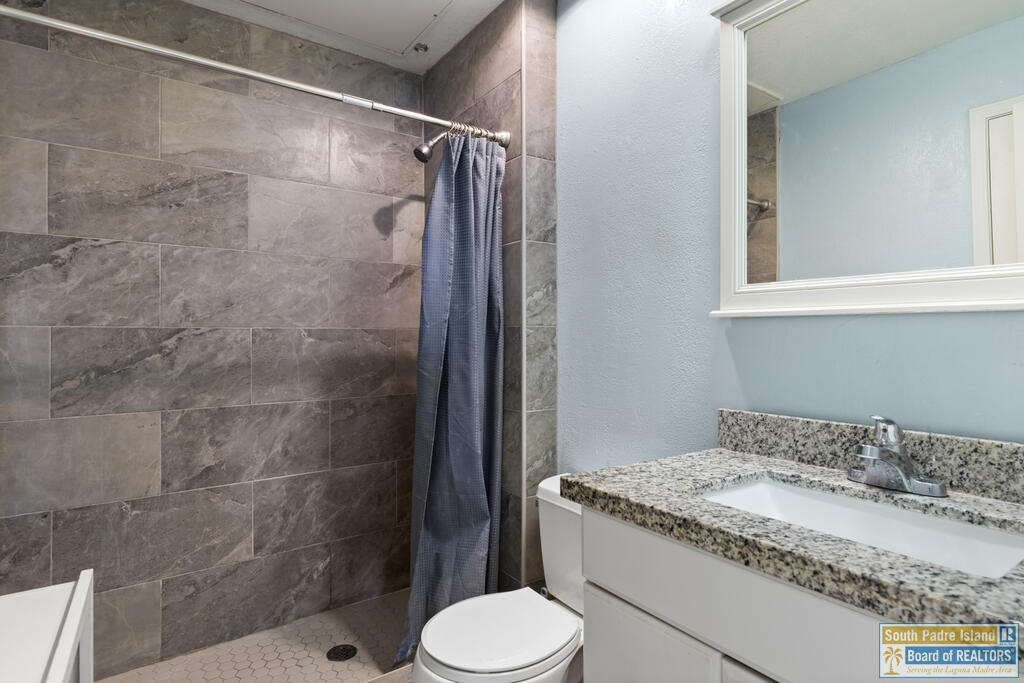 Bathroom with a gray tiled shower, blue curtain, and granite-topped vanity.