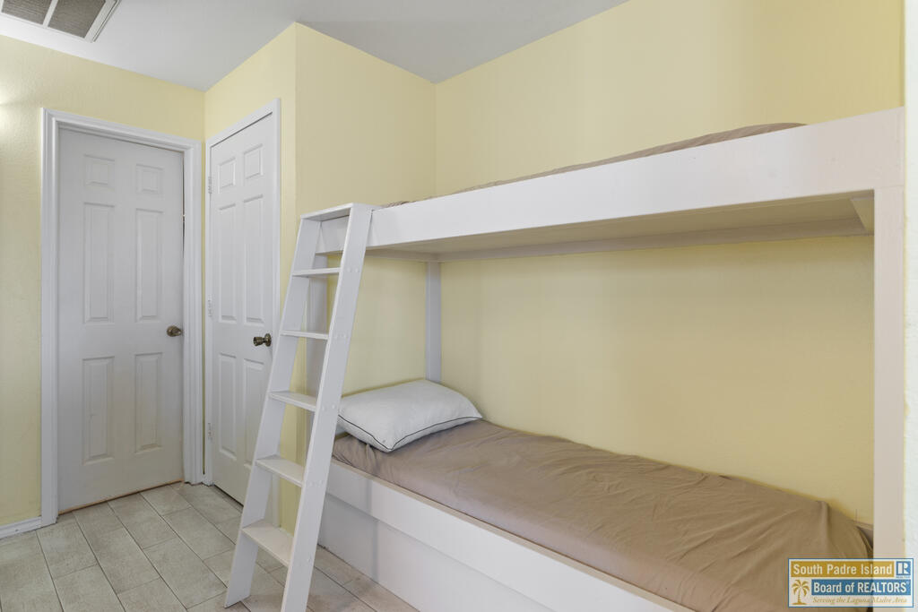 Bedroom with a white bunk bed, tan lower-bunk cover, and ladder against pale yellow walls.