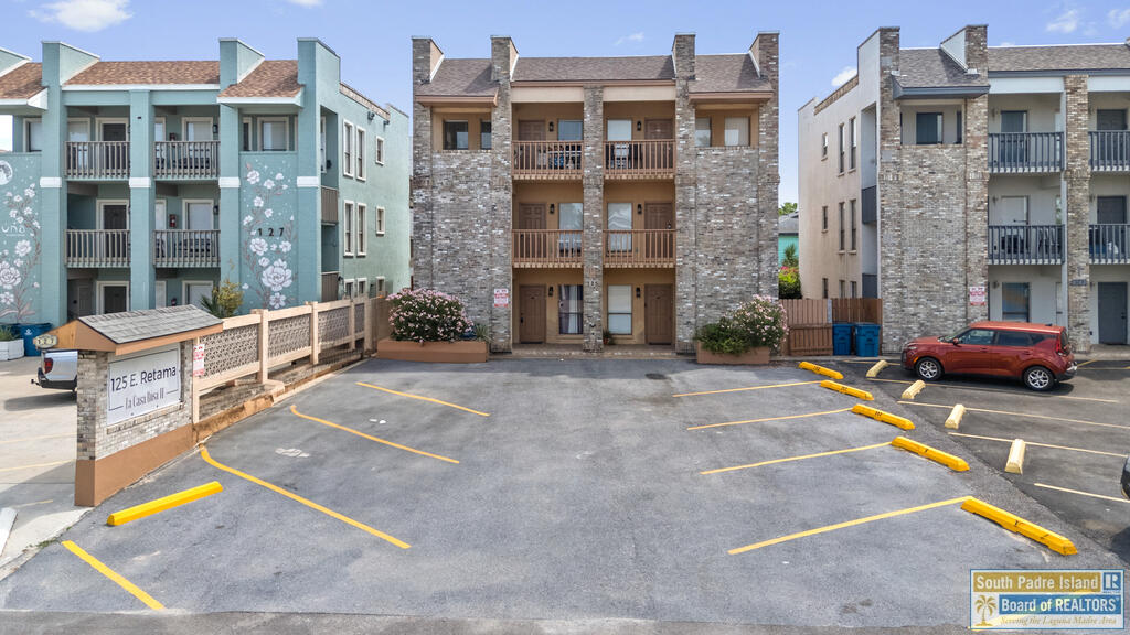 Multi-unit building with brick facades and balconies facing a marked parking lot.