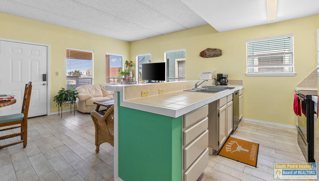 Kitchen and living area with a turquoise peninsula, tiled counters, and a beige sofa.