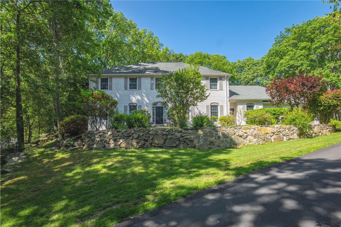 Two-story white brick home behind a stone retaining wall, framed by mature trees.