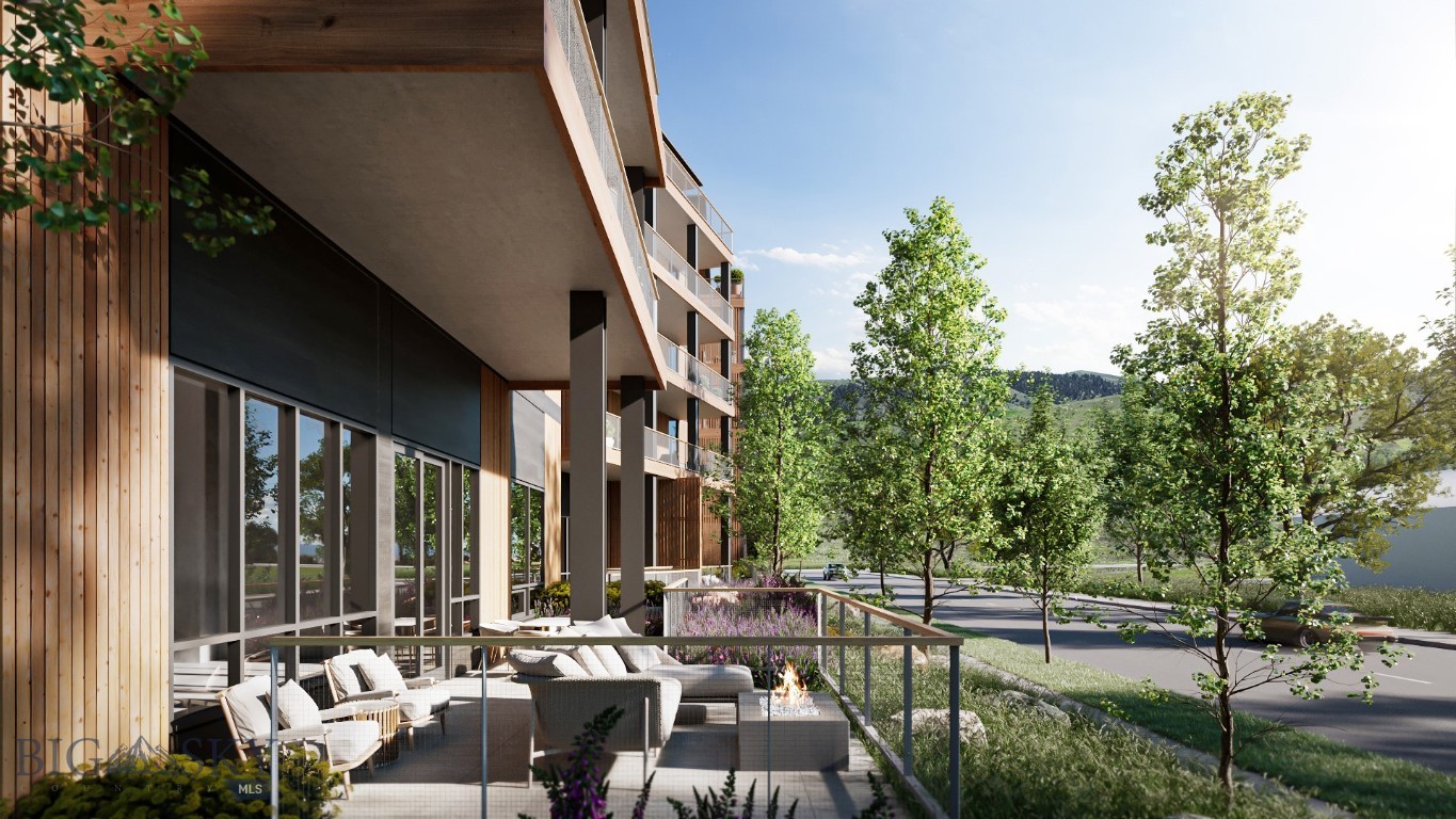Modern residential building with a furnished patio, glass railing, and landscaped grounds.
