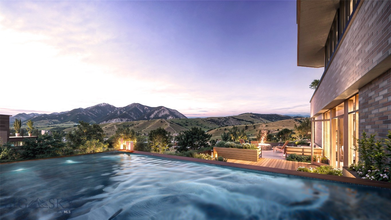 Rooftop pool beside a modern brick building, with a furnished terrace and mountains at dusk.