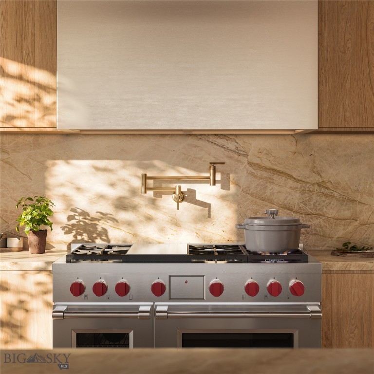 Kitchen range with red knobs beneath a brass pot filler and veined stone backsplash.