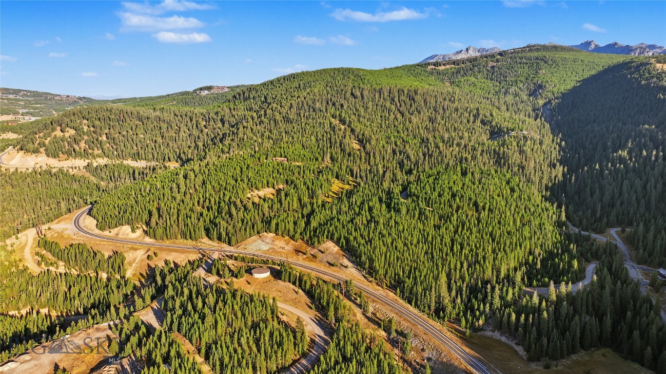 Aerial view of forested mountain terrain near Big Sky, with a winding road and distant peaks.