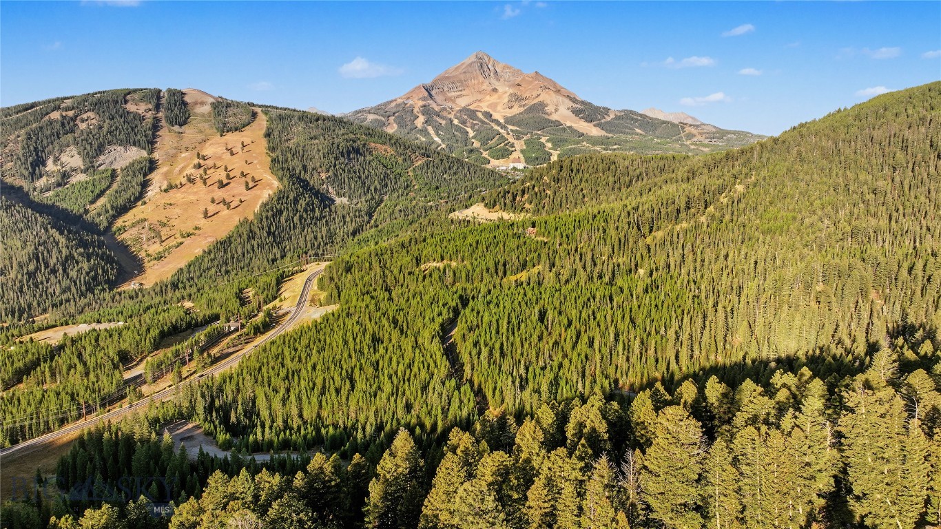 Aerial view of forested mountains near Big Sky, with ski runs and a winding road.