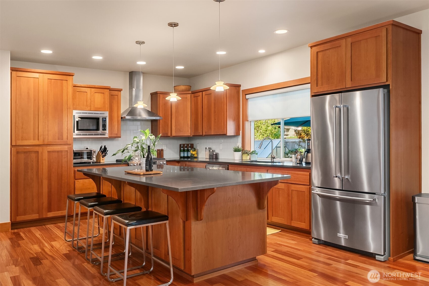 Kitchen with warm wood cabinets, stainless steel appliances, and a large island with four stools.