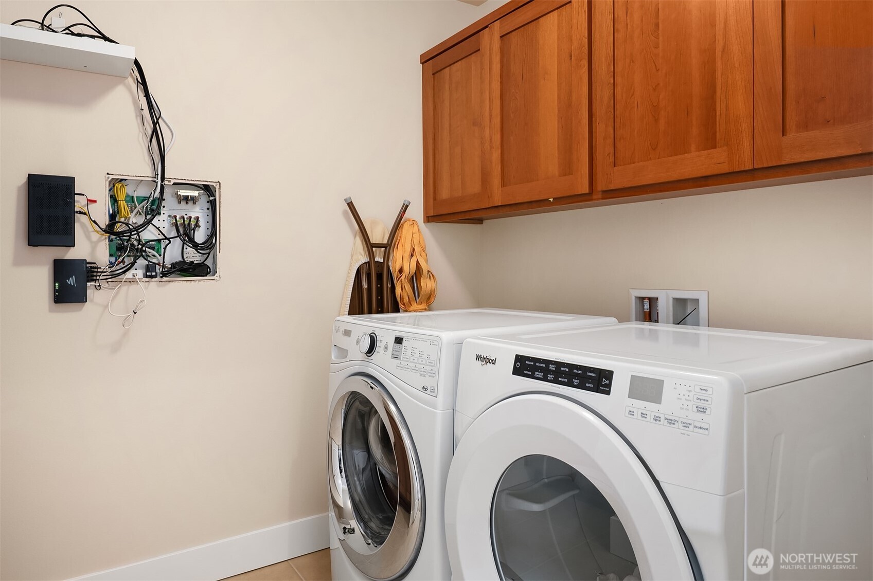 Laundry room with front-loading washer and dryer beneath warm wood cabinets.