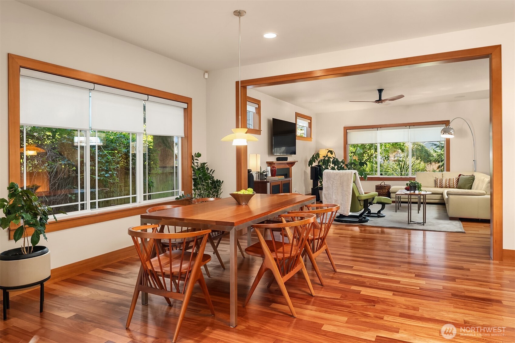 Dining and living area with wood floors, large windows, and a wooden dining table.