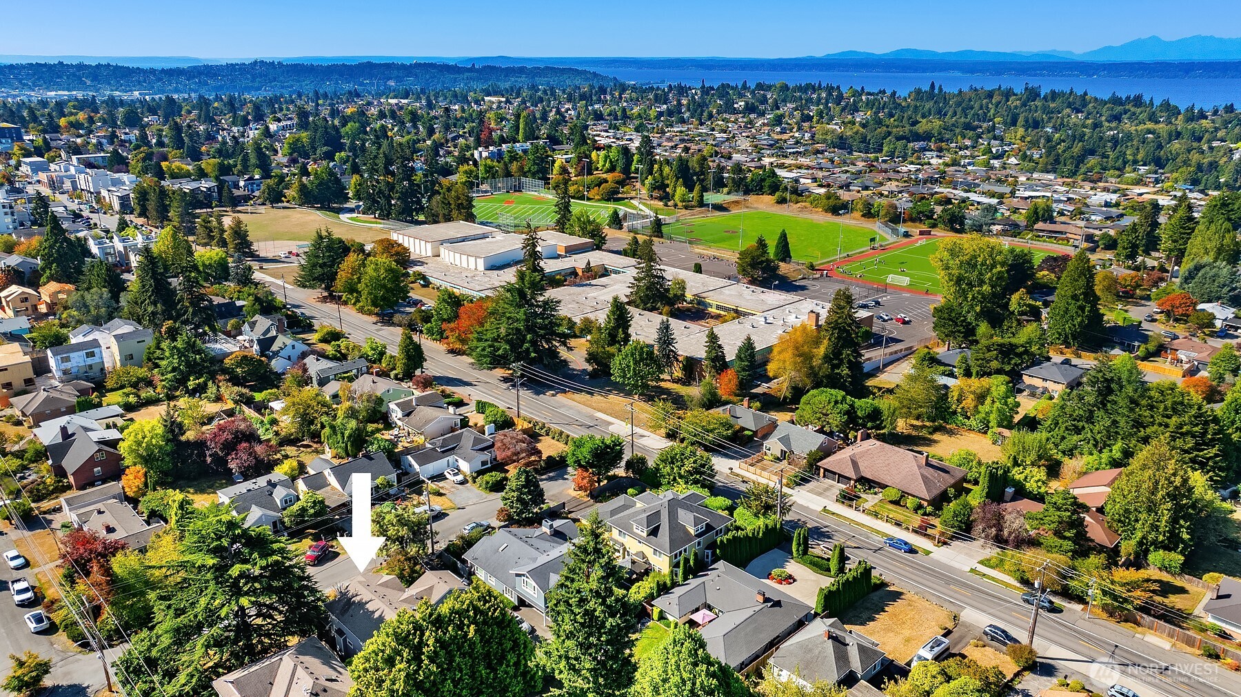 Aerial neighborhood view with an arrow marking the home, near school sports fields and water.