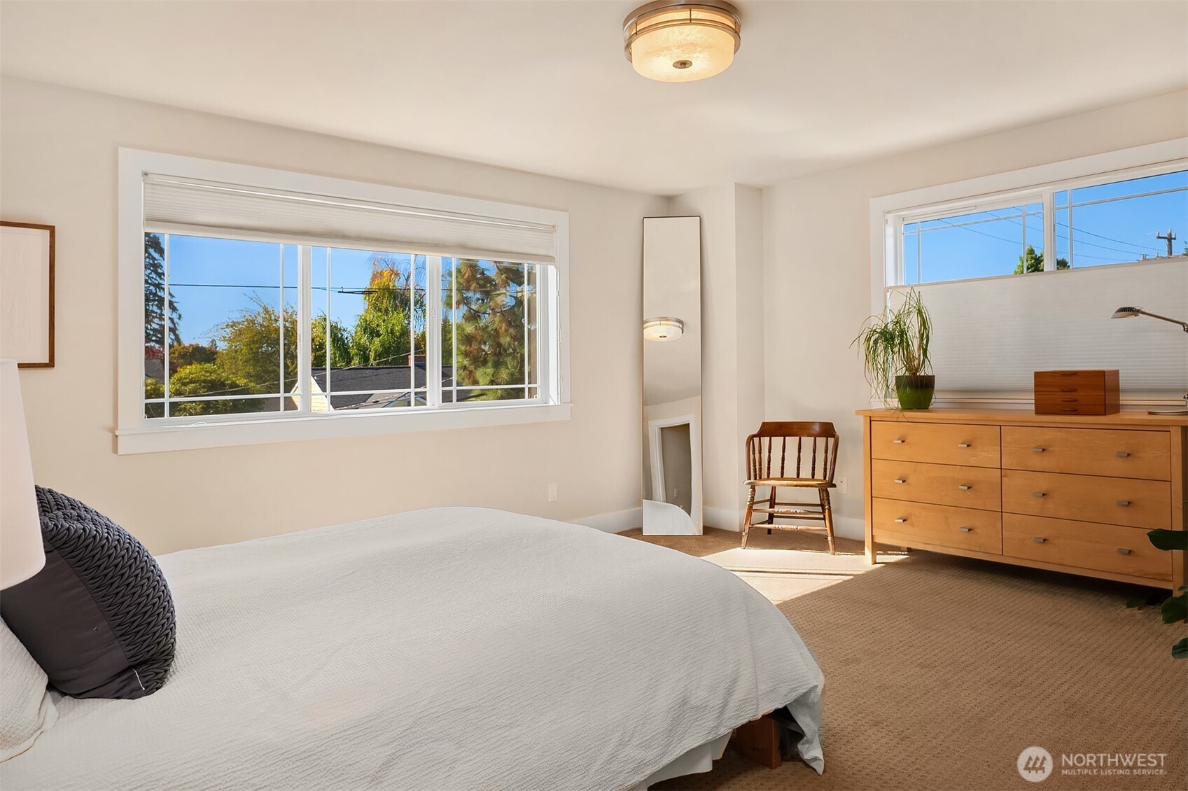 Furnished bedroom with a large bed, wide windows, and a wooden dresser.