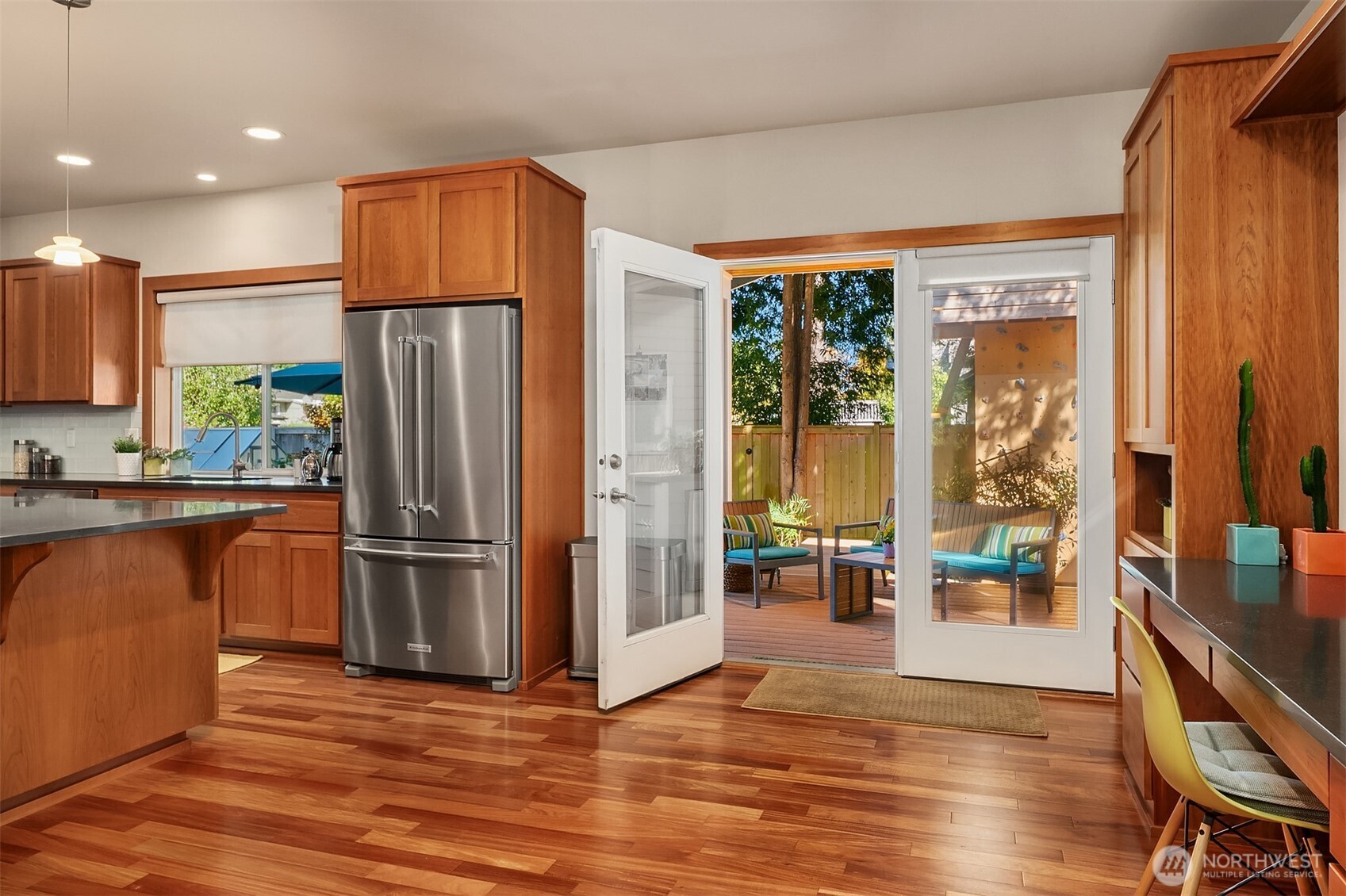 Kitchen with wood cabinetry and hardwood floors, opening through French doors onto a furnished deck.