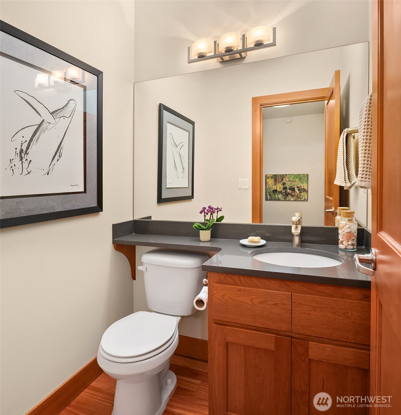 Bathroom with a wood vanity, dark countertop, oval sink, and white toilet.