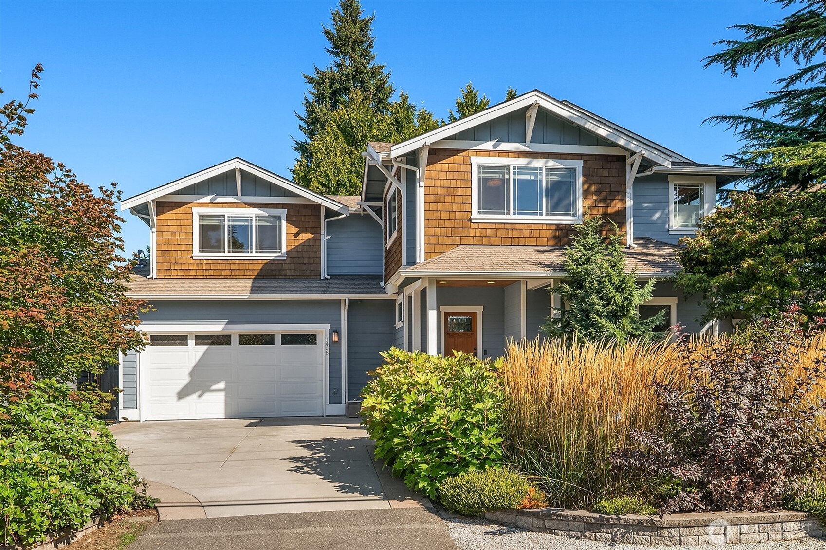 Two-story blue house with brown shingle accents, a double garage, and landscaped front yard.