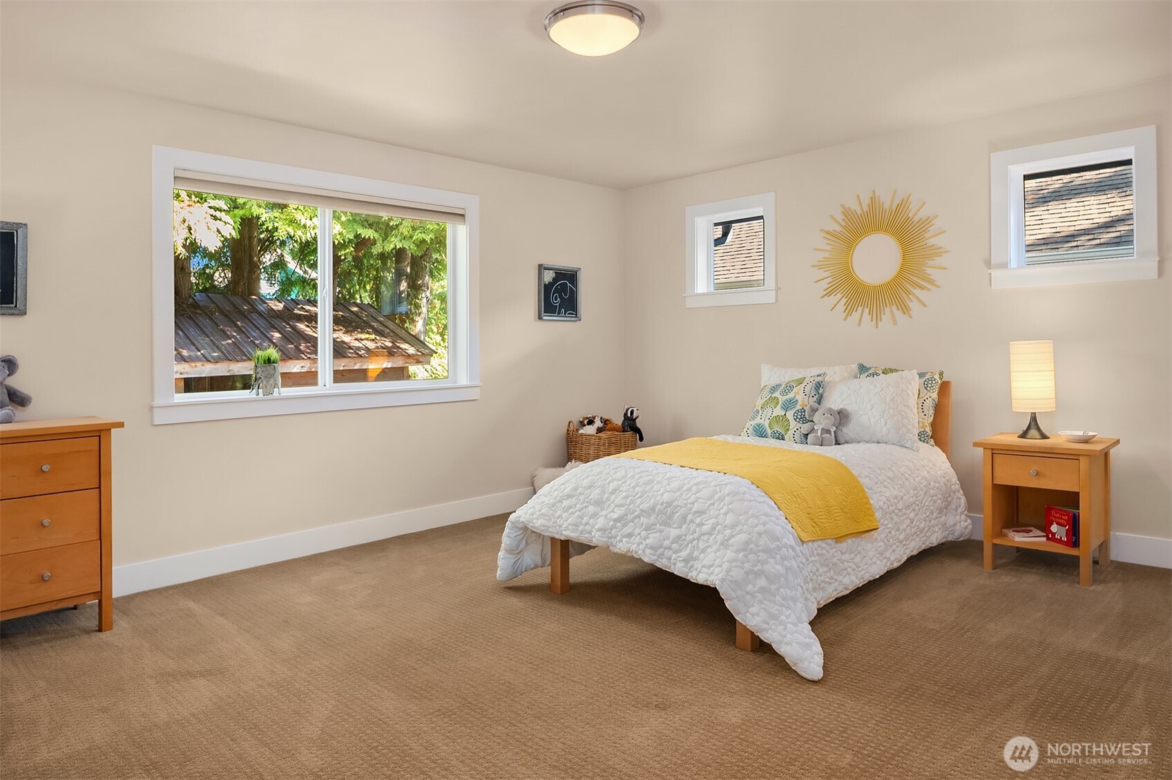 Furnished bedroom with a white quilted bed, yellow throw, and large window overlooking trees.