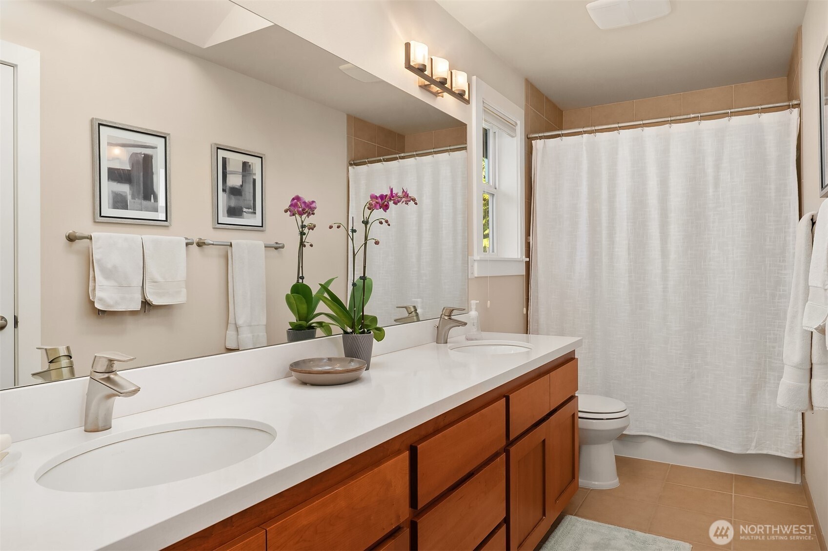 Bathroom with a long double-sink vanity, warm wood cabinetry, large mirror, and white shower curtain.