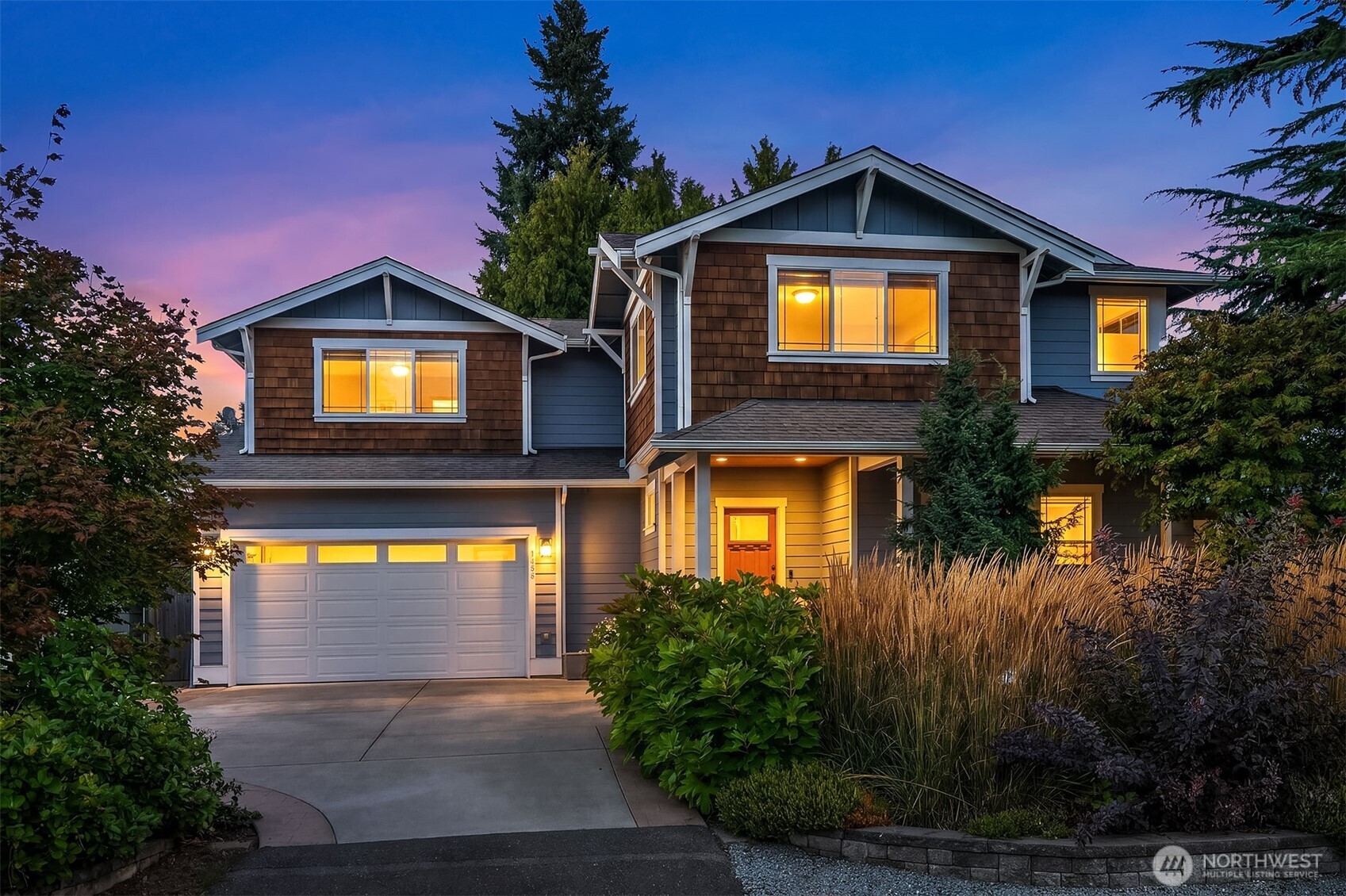 Two-story house at dusk with warmly lit windows, a double garage, and landscaped front garden.