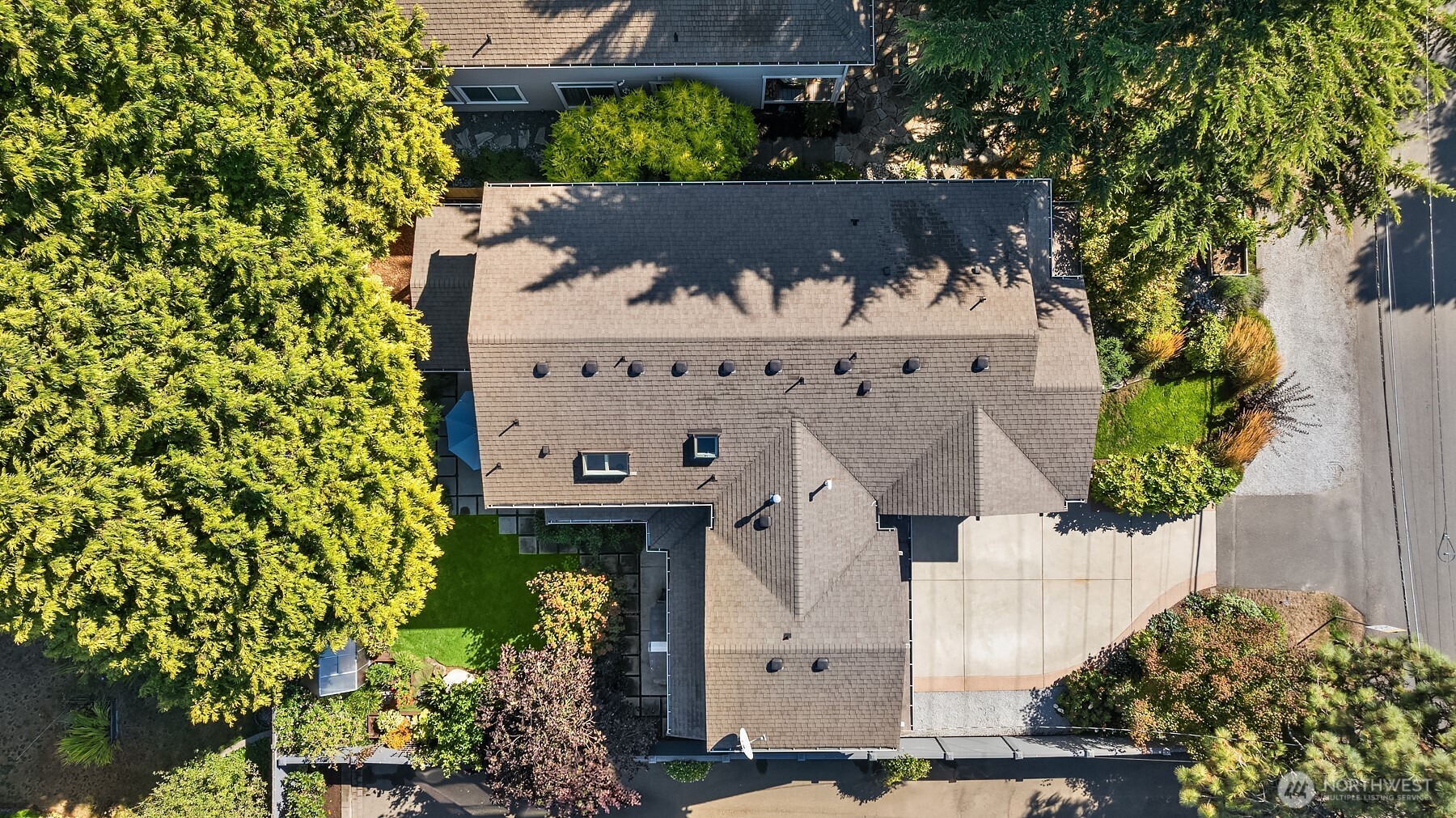 Aerial view of a house with a broad shingle roof, landscaped yard, and concrete driveway.