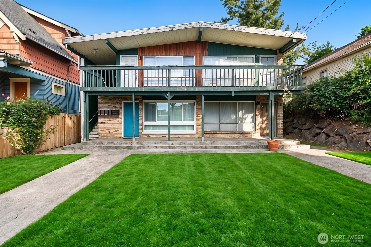 Two-story home with a broad green-trimmed balcony, brick lower facade, and blue front door.
