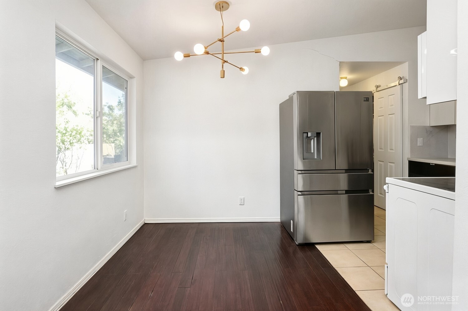 Unfurnished kitchen with dark wood floors, a large window, stainless steel refrigerator, and brass pendant light.