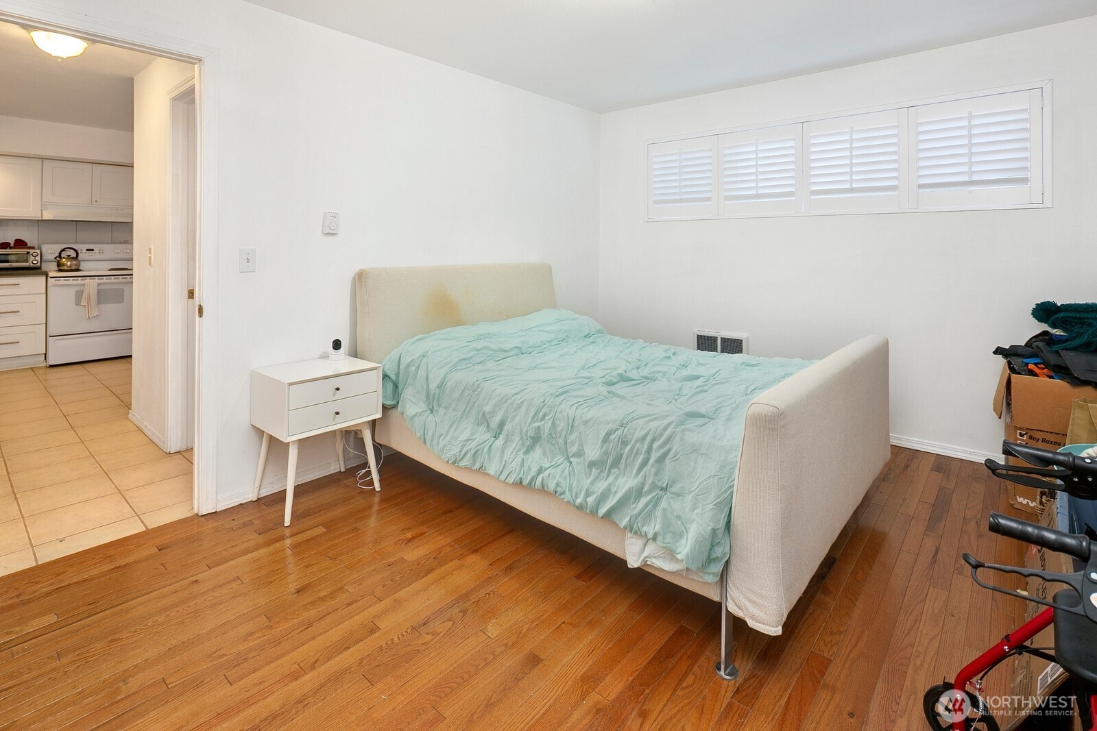 Bedroom with a cream bed, pale aqua bedding, shuttered windows, and an open view into the kitchen.