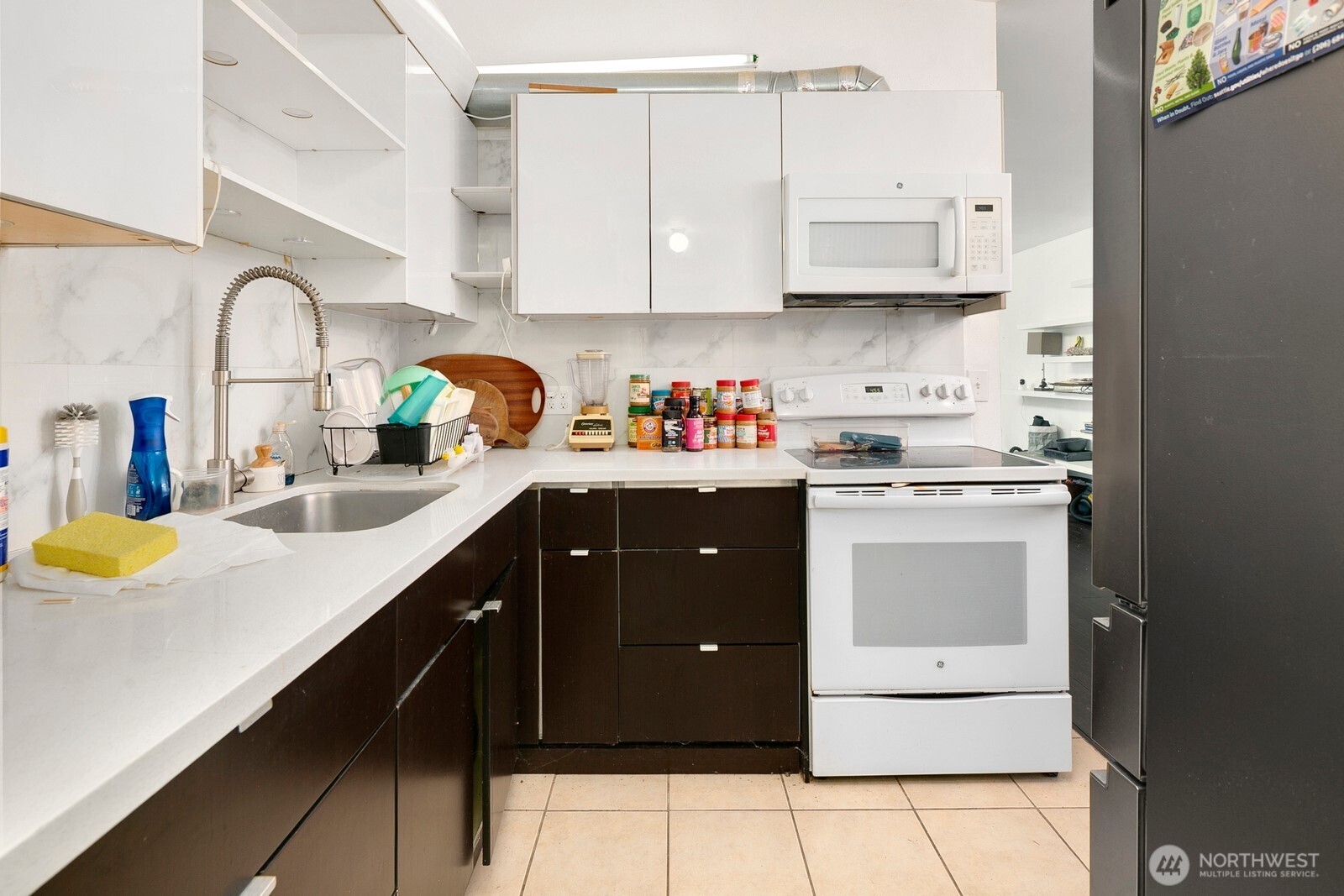 Compact kitchen with dark cabinets, white counters, a white range, and a tall spring-coil faucet.