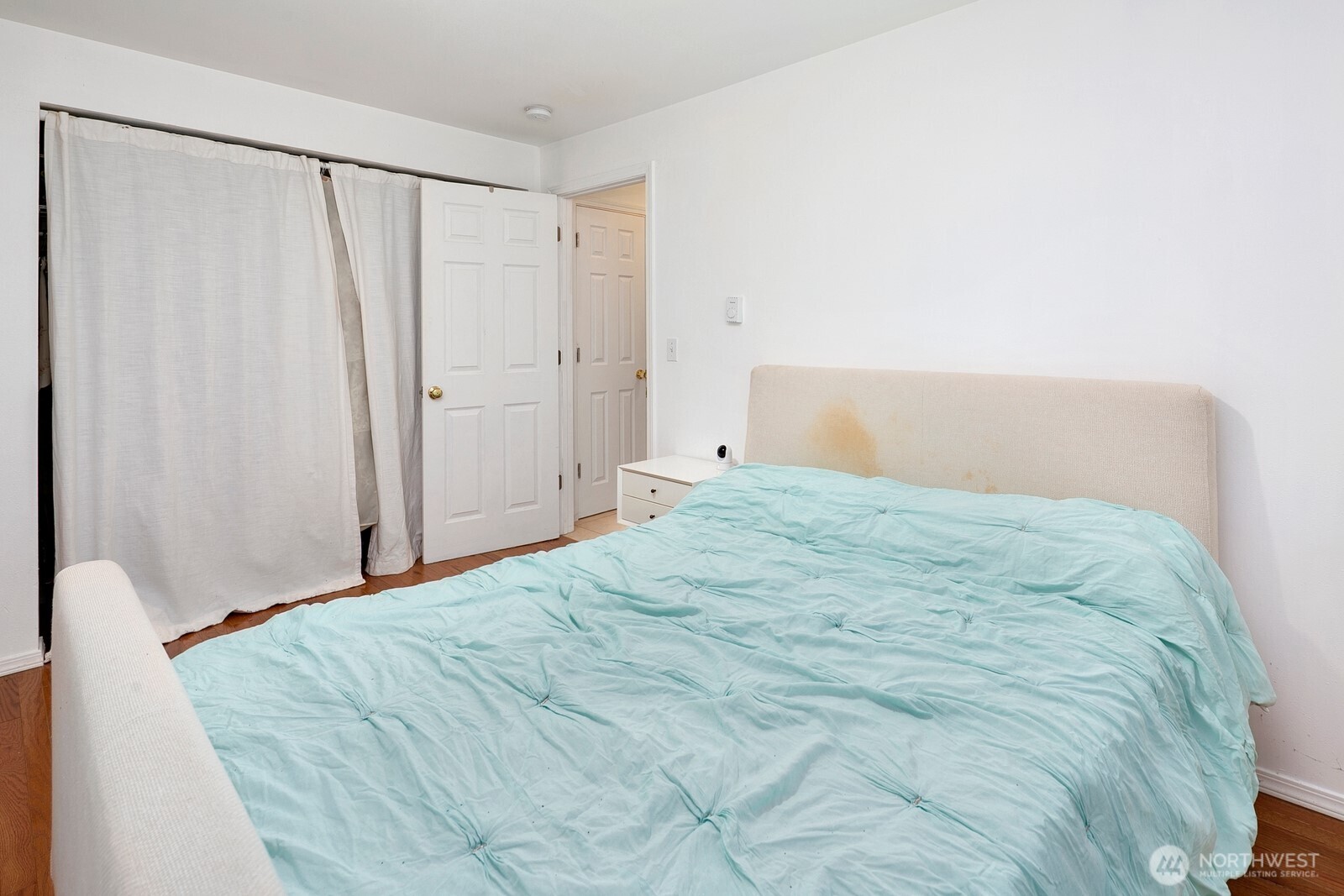 Bedroom with a large bed covered in pale aqua bedding and a stained beige headboard.