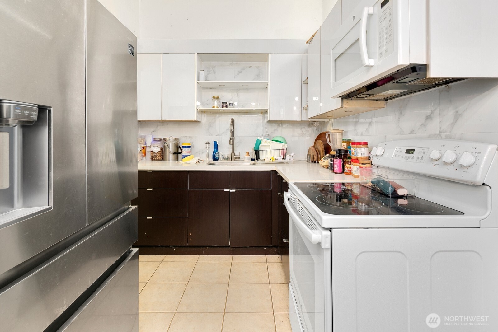 Compact kitchen with stainless-steel refrigerator, dark lower cabinets, and white electric range.