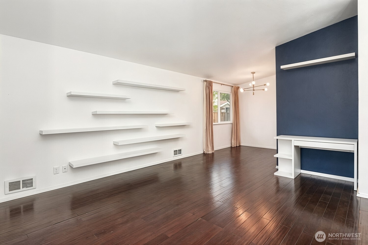 Empty living room with dark hardwood floors, floating shelves, and a navy-blue accent wall.
