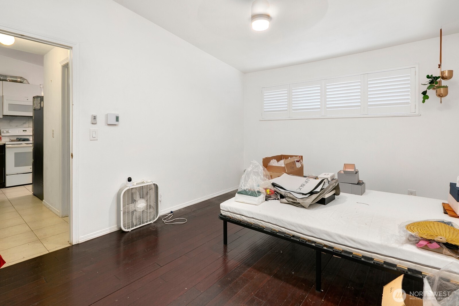 Bedroom with dark hardwood floors, a high louvered window, and a mattress on a low frame.