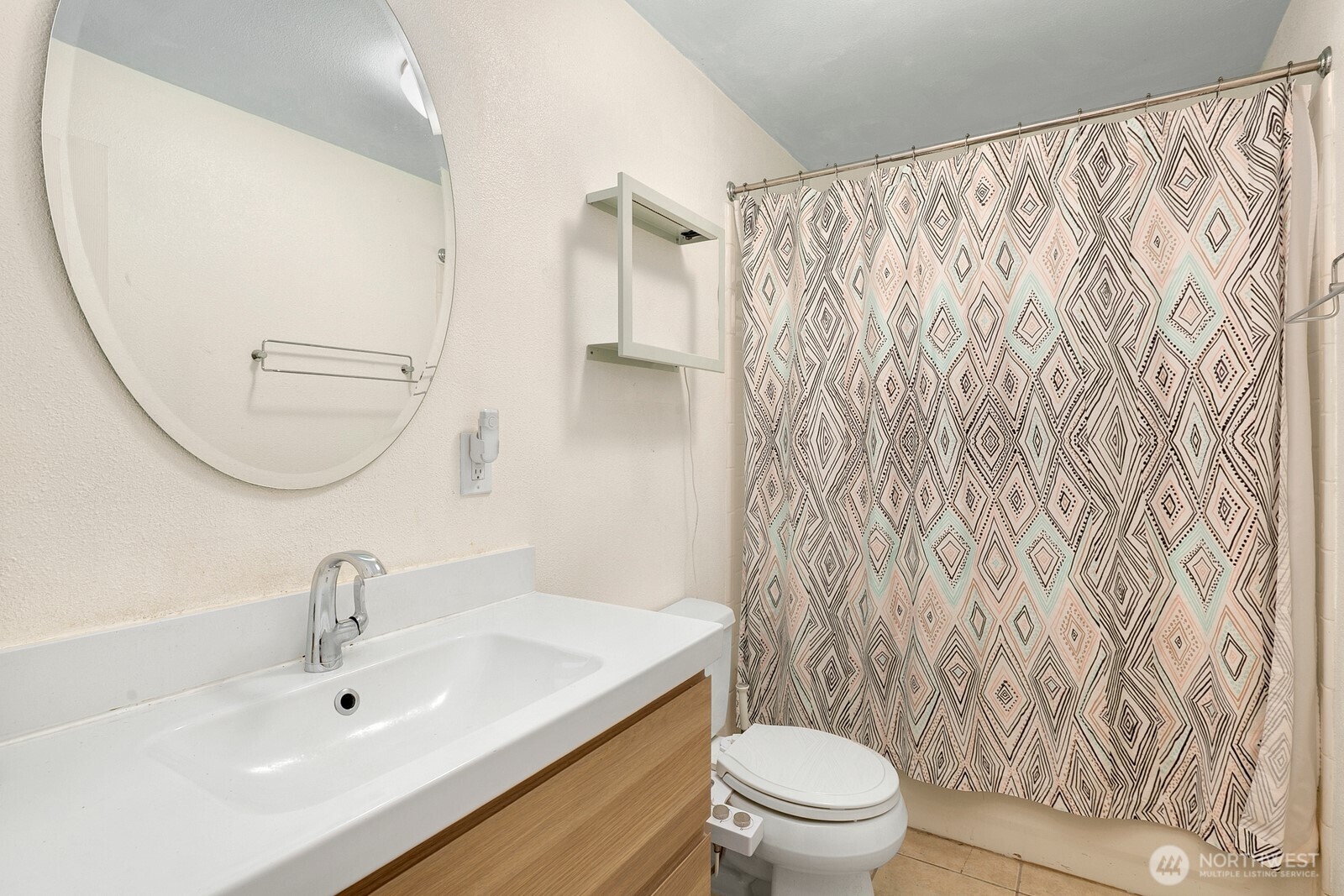 Bathroom with a white sink and wood vanity, round mirror, and geometric shower curtain.
