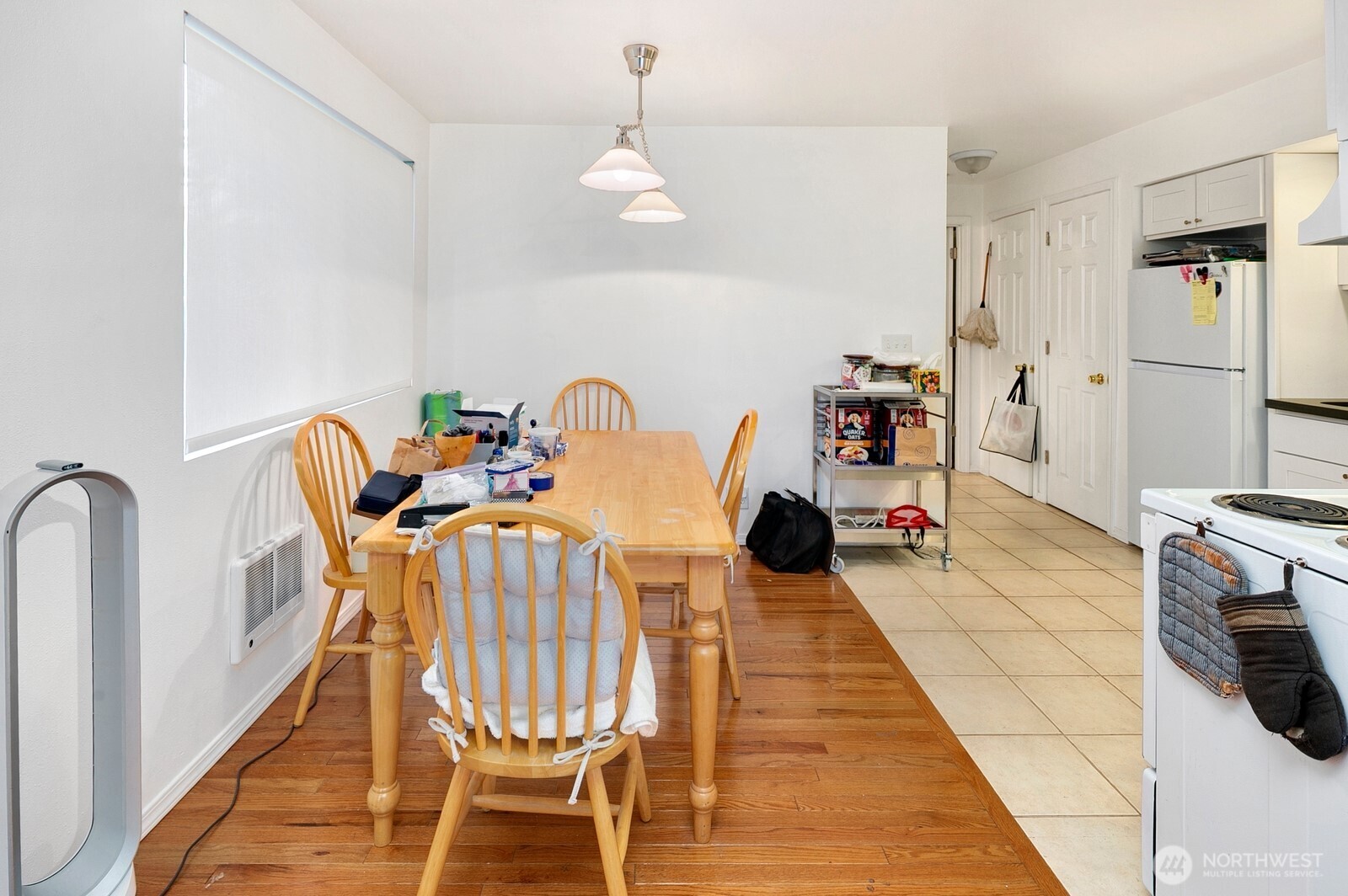Kitchen dining area with a wooden table, hardwood flooring, white cabinets, and tiled floor.