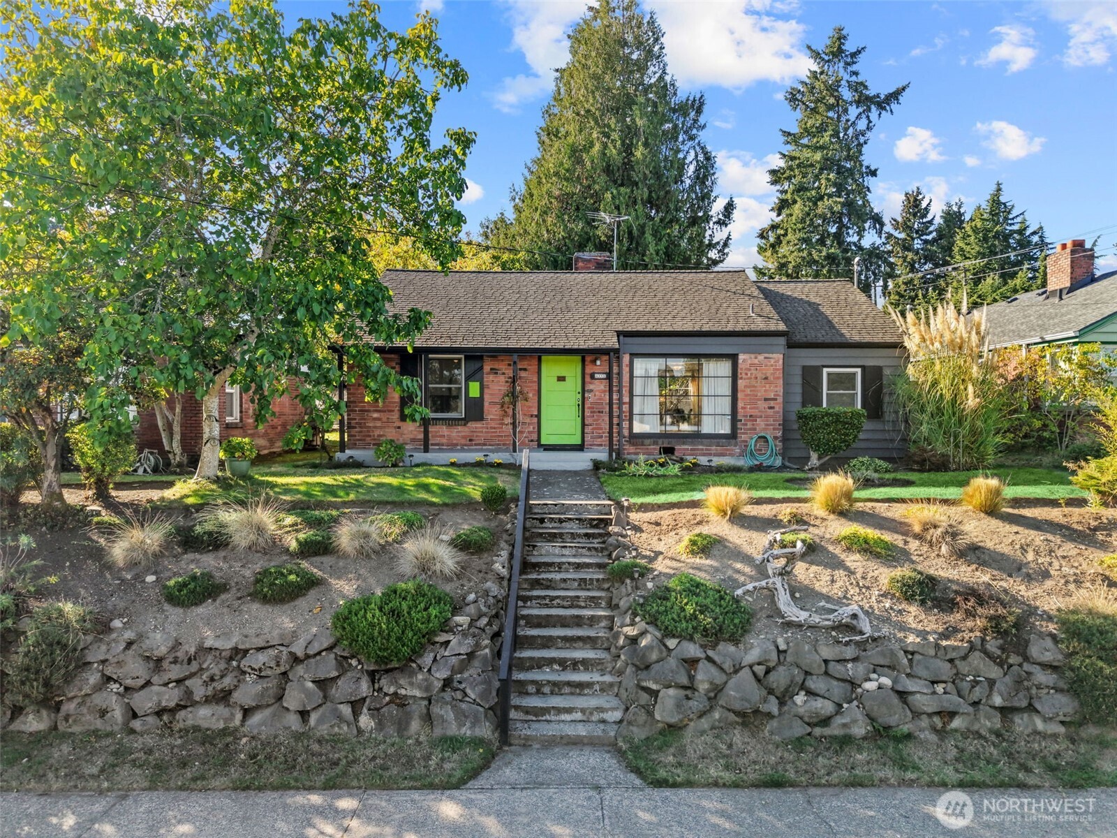 Single-story brick home with a bright green front door and stone steps through a landscaped yard.