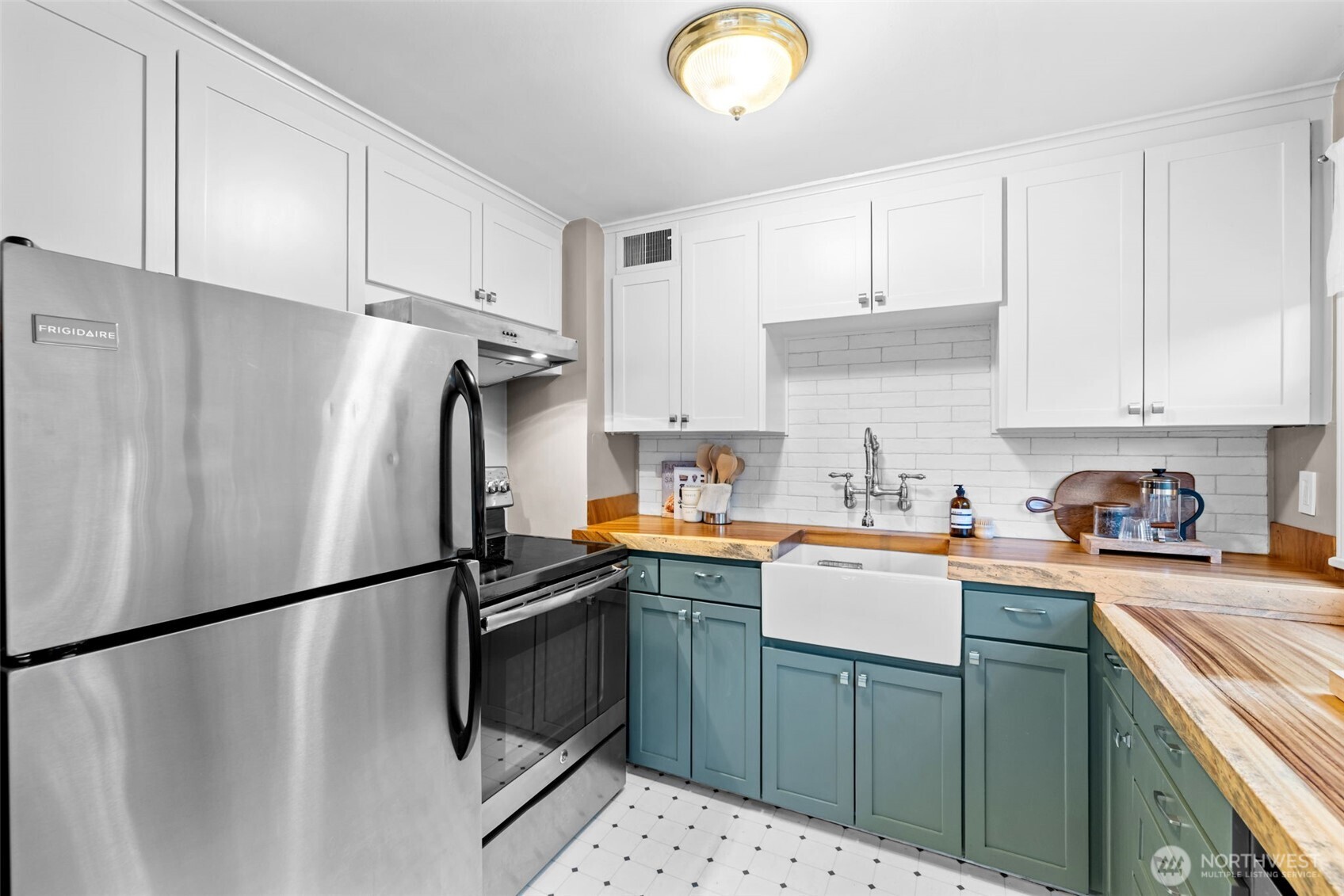Kitchen with blue-green cabinets, butcher-block counters, farmhouse sink, and stainless steel appliances.