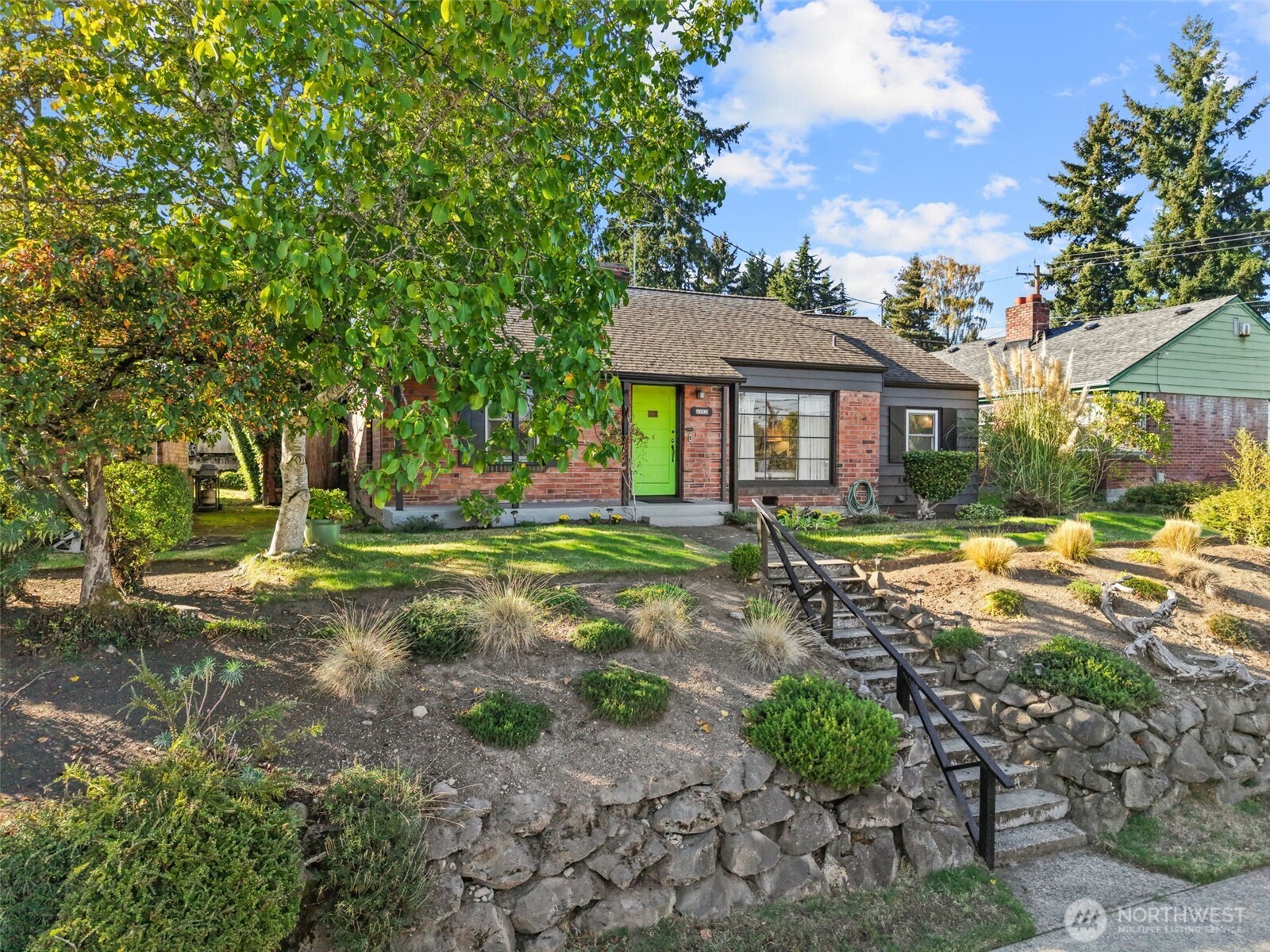 Brick Seattle home with a bright green front door, mature trees, and stone terraced landscaping.