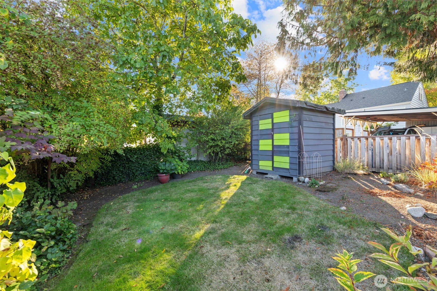 Backyard with a lime-paneled shed, lawn, mature trees, and covered carport.