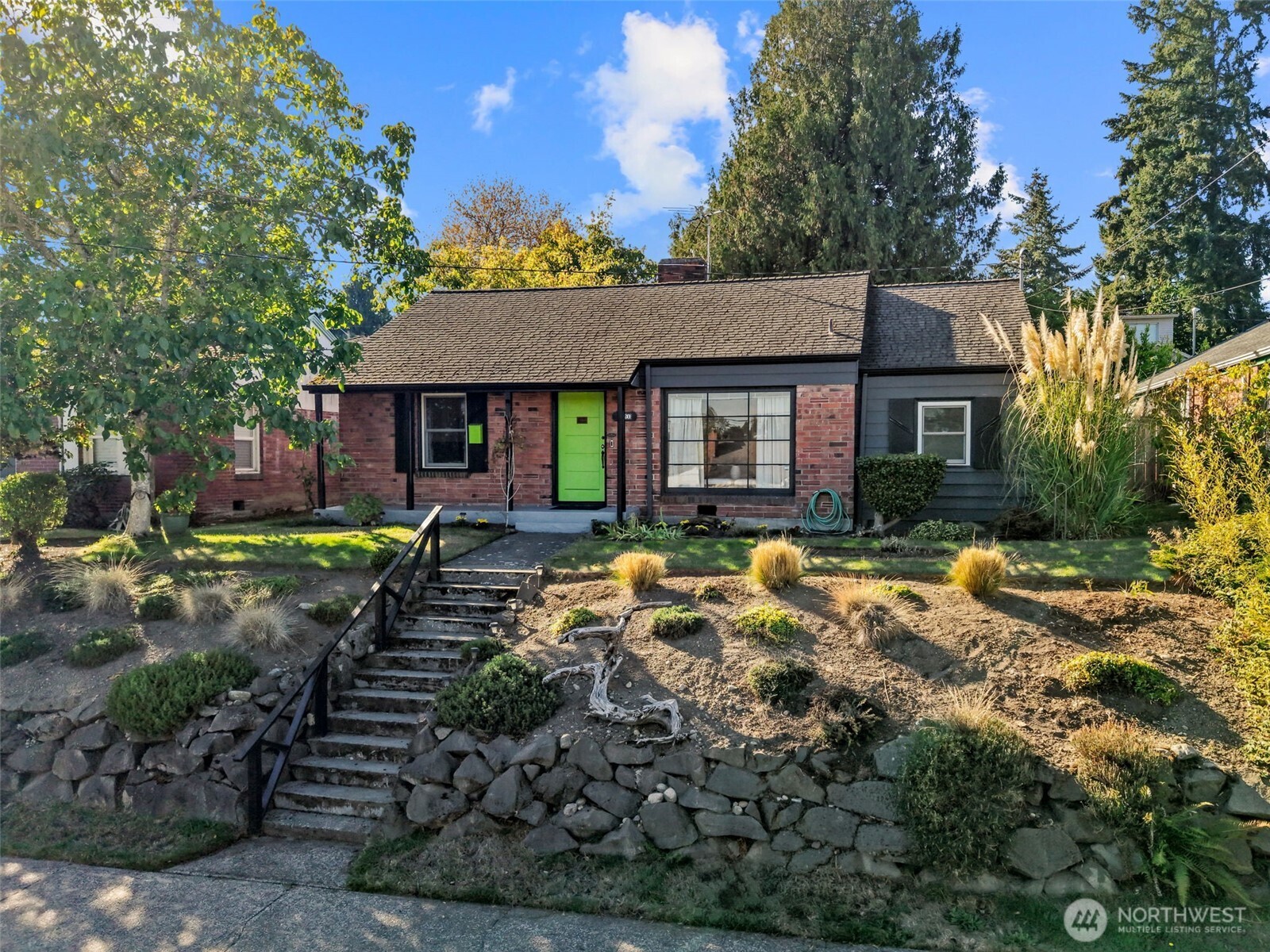 Brick house with a bright green front door above stone steps and a landscaped terraced yard.