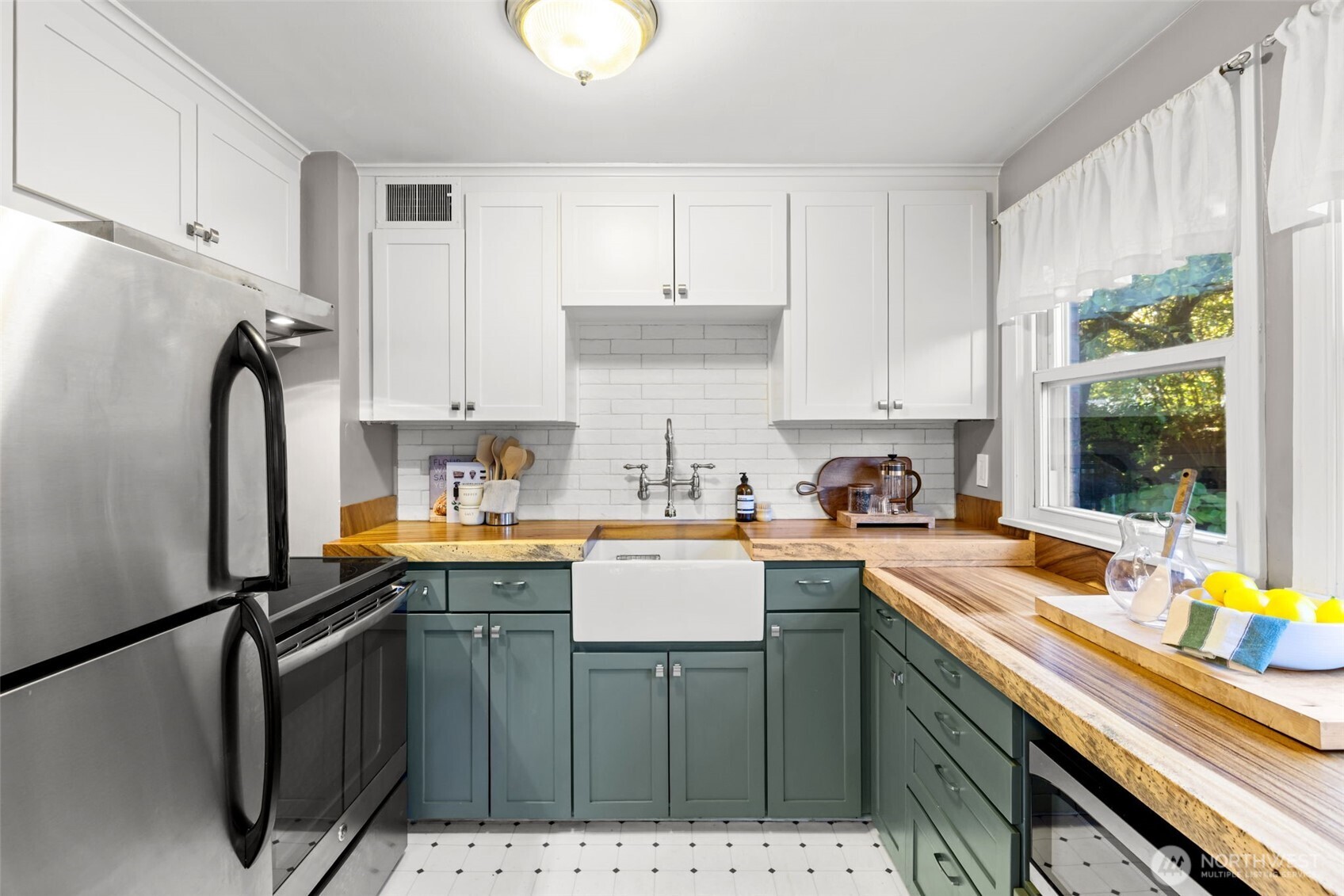Kitchen with sage-green cabinets, butcher-block counters, farmhouse sink, and stainless-steel appliances.