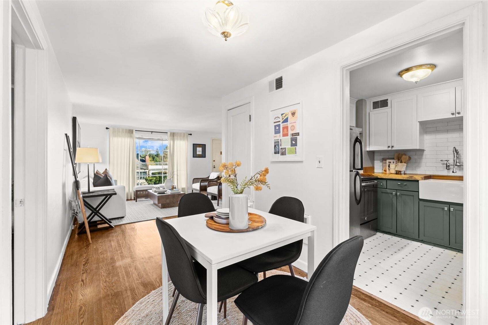 Dining area with a white table opens to a bright living room and a kitchen with green cabinets.