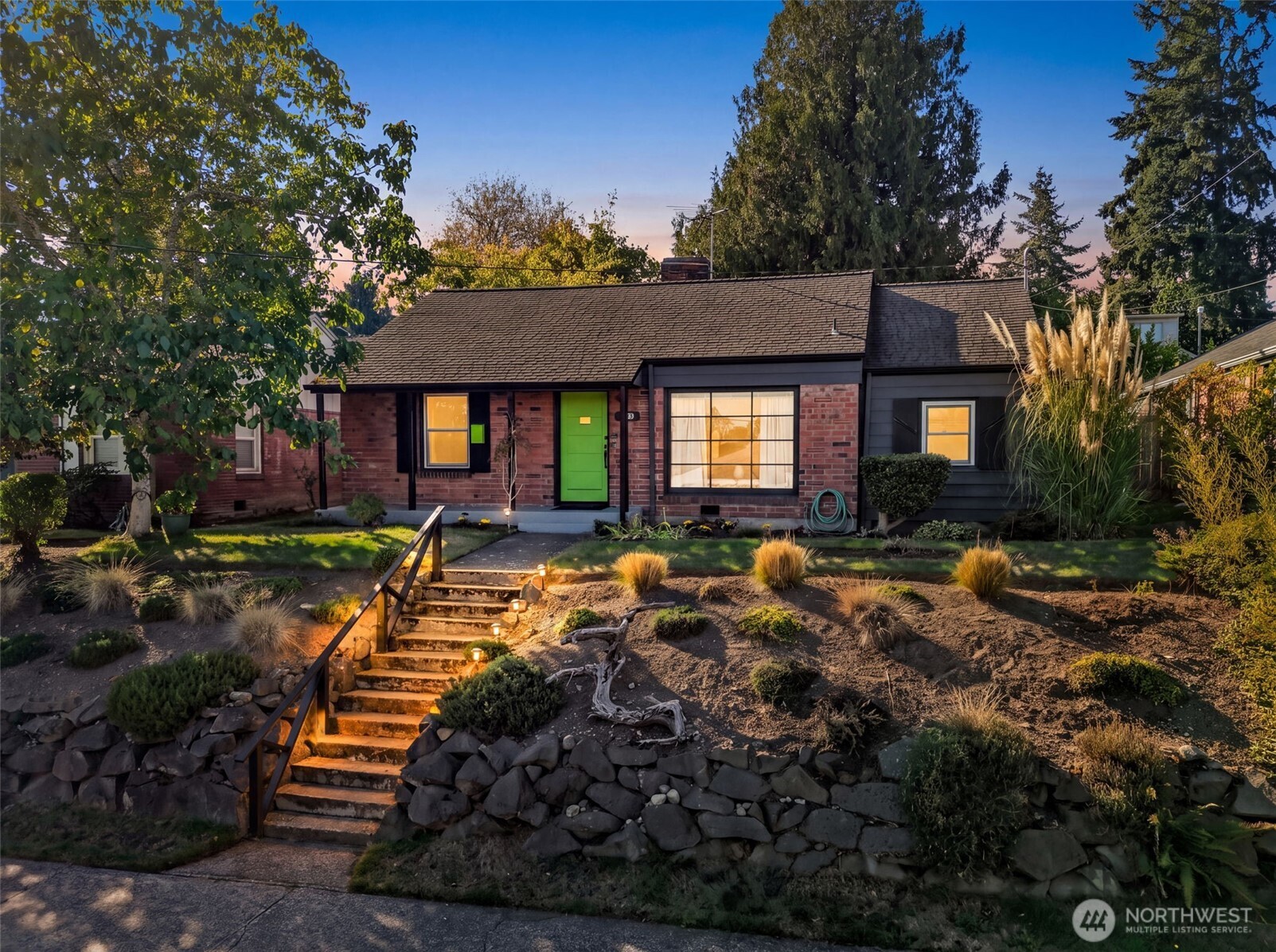 Brick-and-siding home with a bright green front door, broad entry window, and terraced garden stairs.