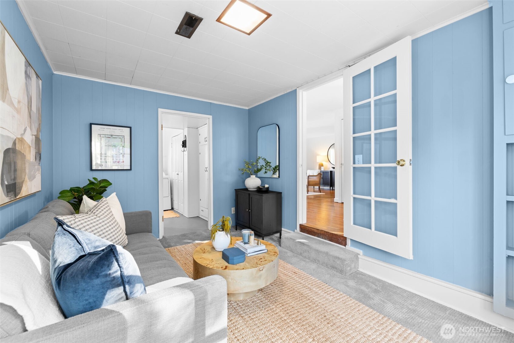 Staged living room with blue paneled walls, a gray sofa, and open French doors.