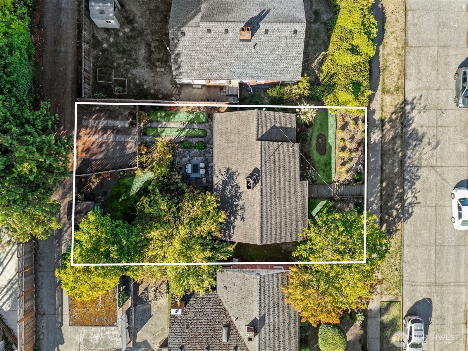 Aerial view of a house and landscaped lot outlined in white, with mature trees and a paved patio.