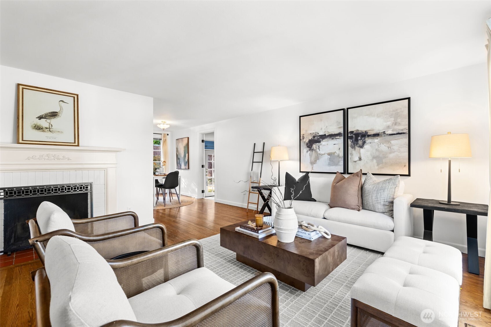 Staged living room with a white sofa, fireplace, hardwood floors, and a pale patterned rug.