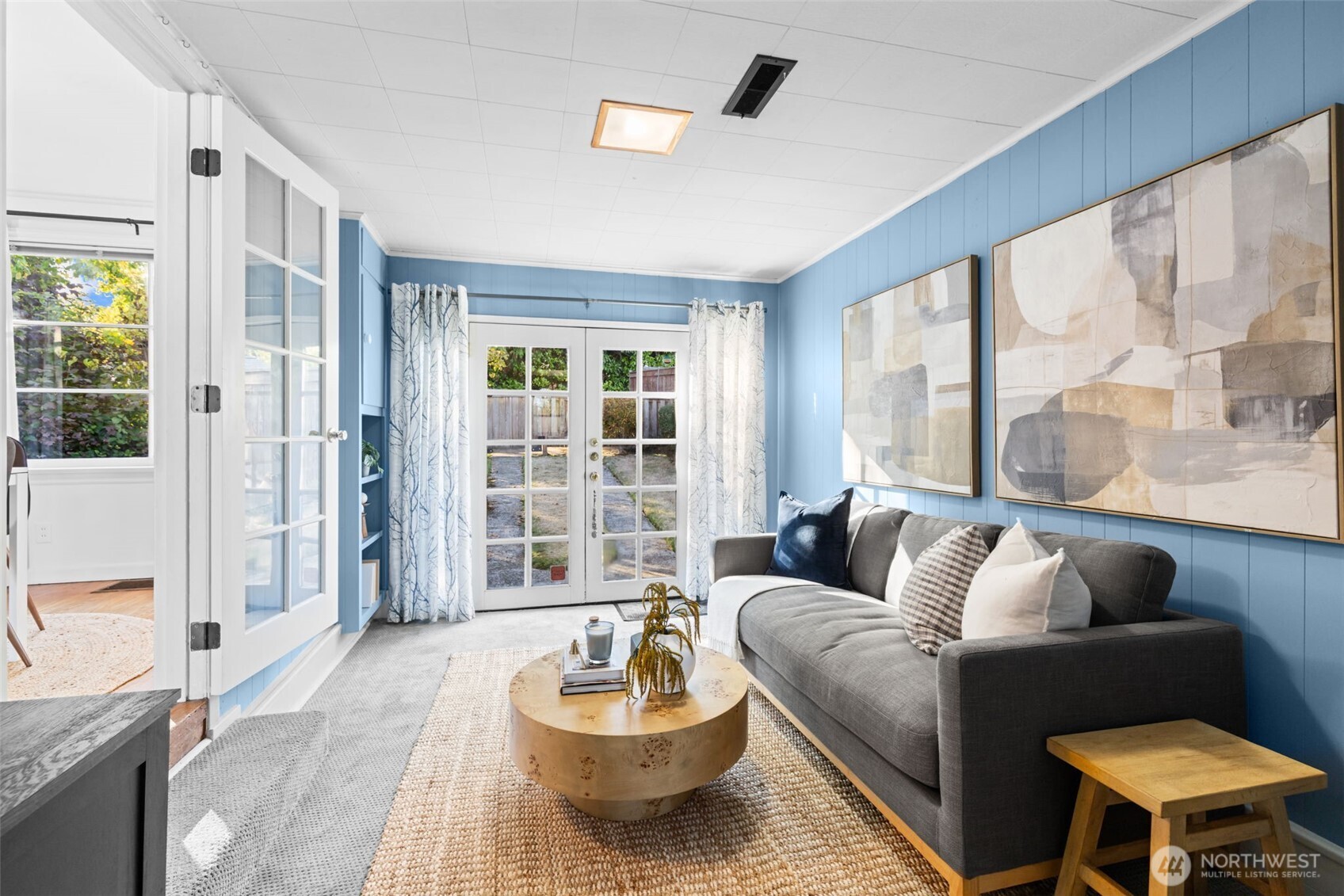 Staged living room with blue walls, a gray sofa, and French doors to the yard.