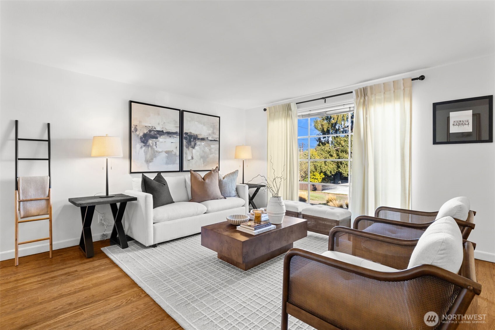 Staged living room with a white sofa, cane armchairs, and a large window overlooking trees.
