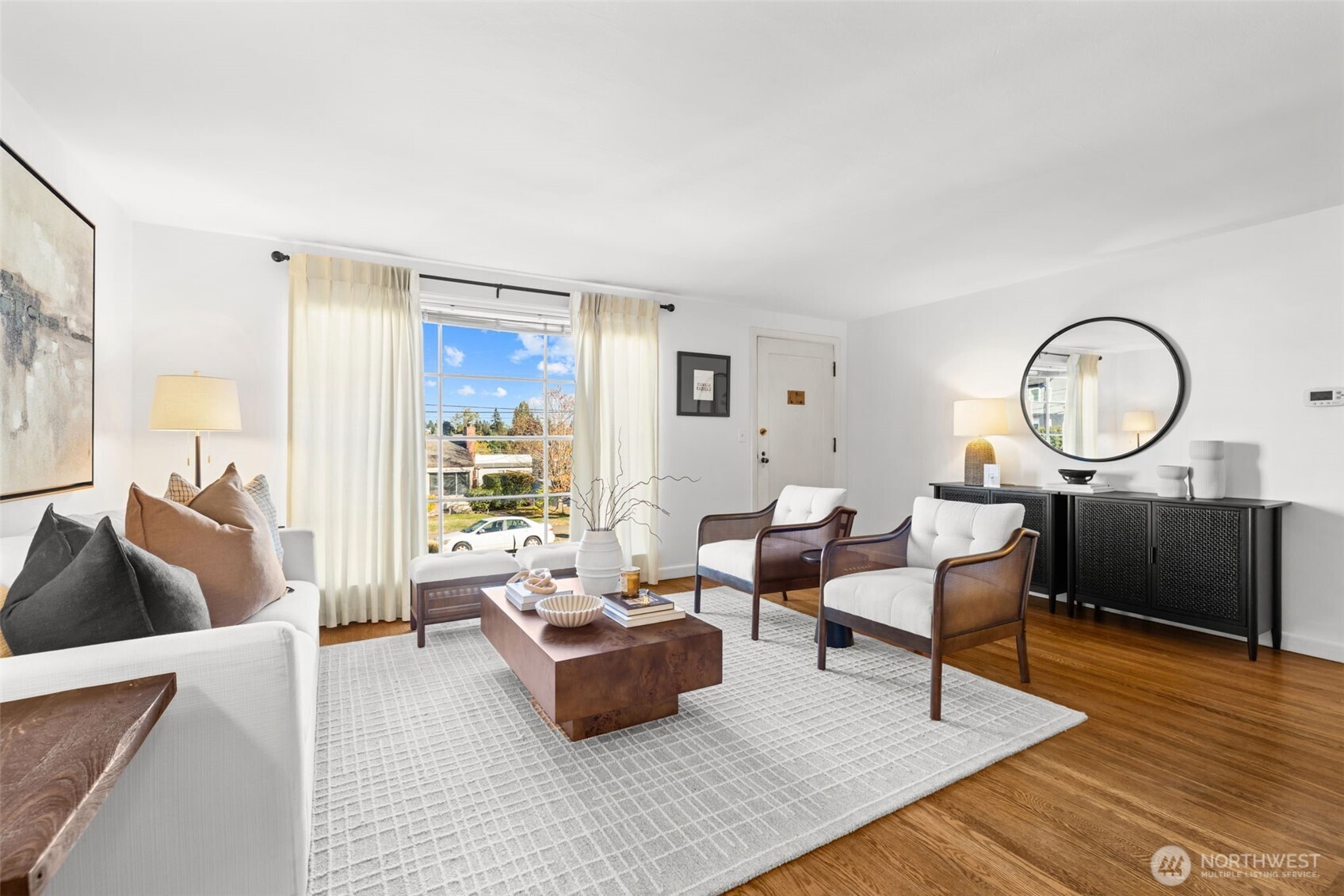 Staged living room with white seating, a wood coffee table, and a large curtained window.