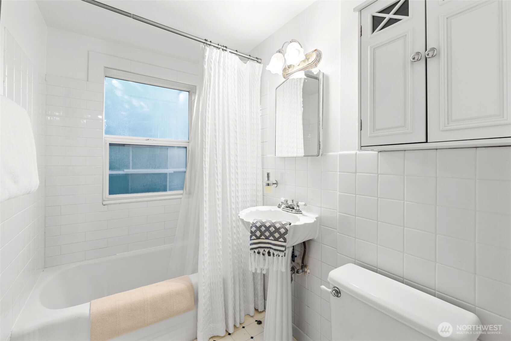 White bathroom with a bathtub, pedestal sink, and tiled walls.